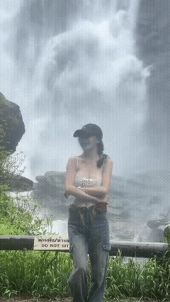 穿着黑帽子和白顶的女人站在瀑布前面。