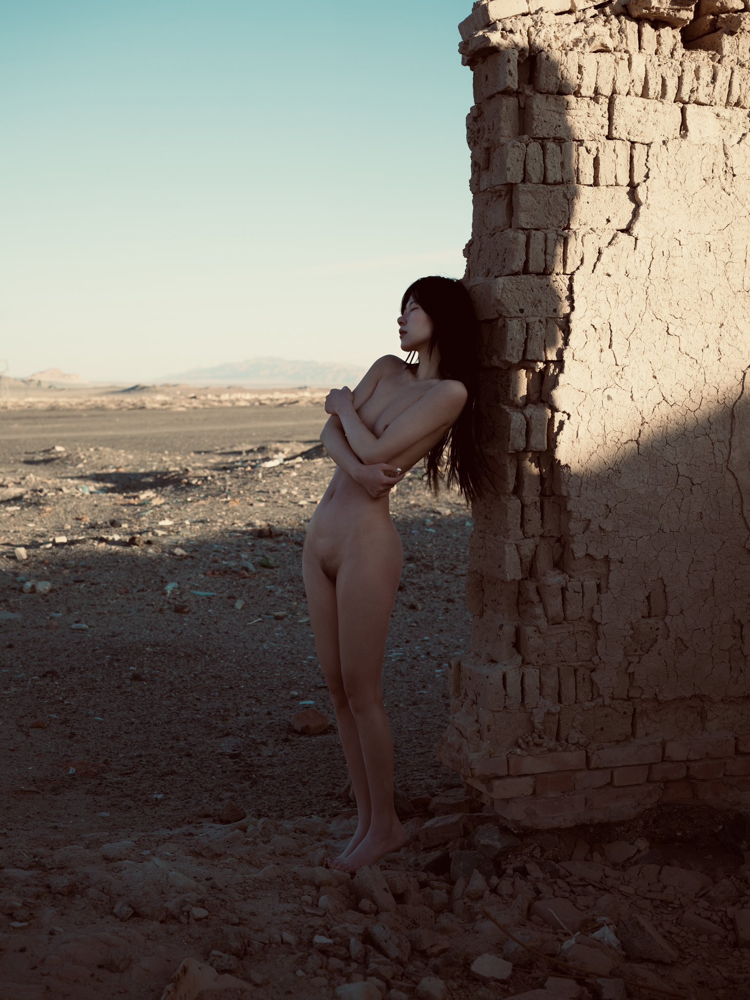 裸体的女人站在砖墙前。