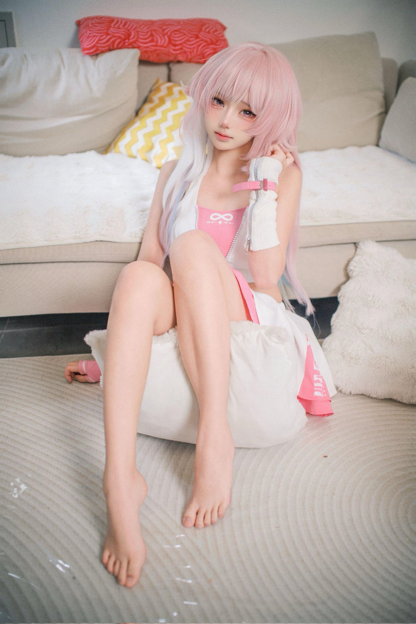 一位穿着粉红色口音的白色裙子的女孩坐在沙发上。