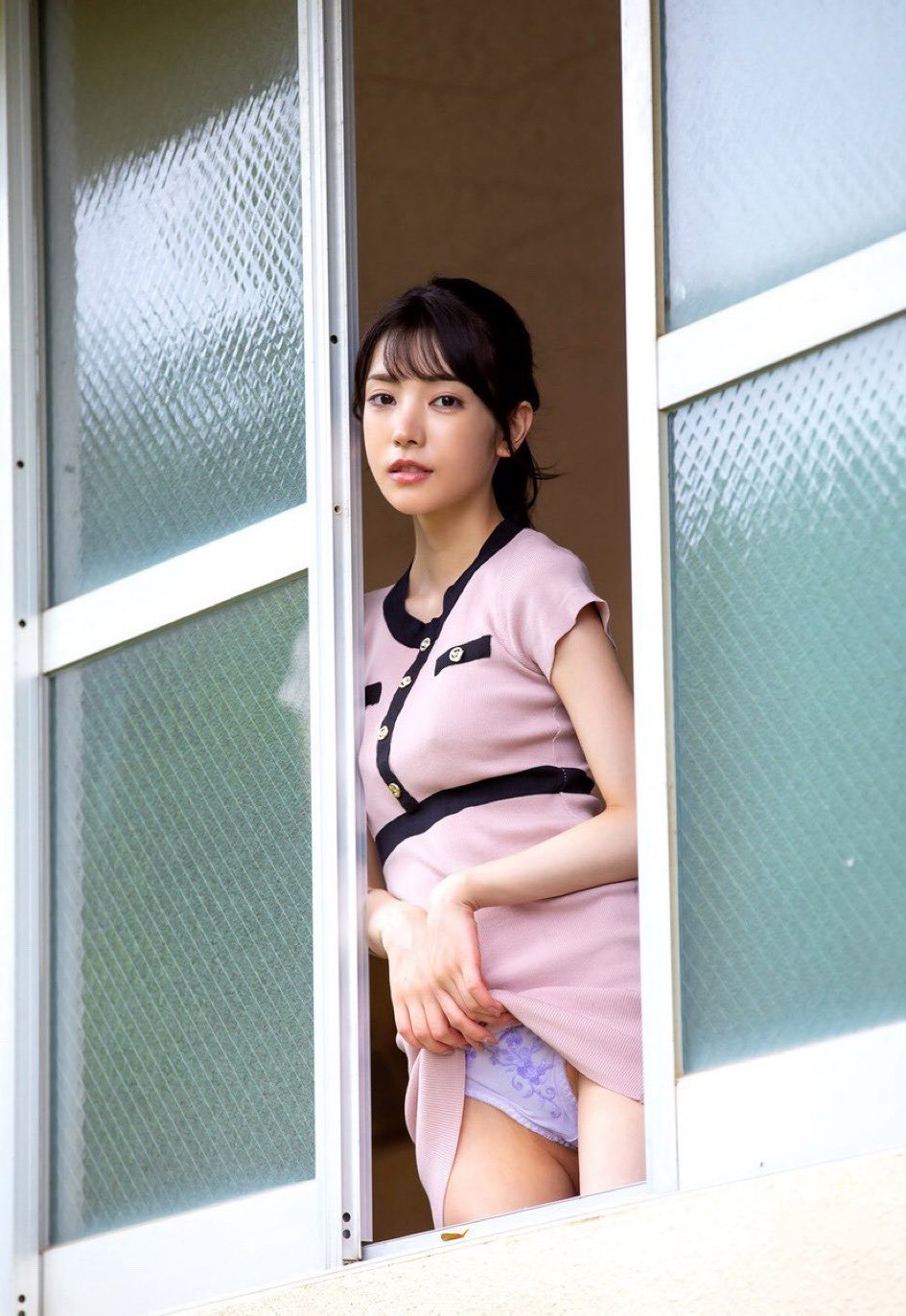 穿着粉红色裙子和黑色带的女人站在窗前。