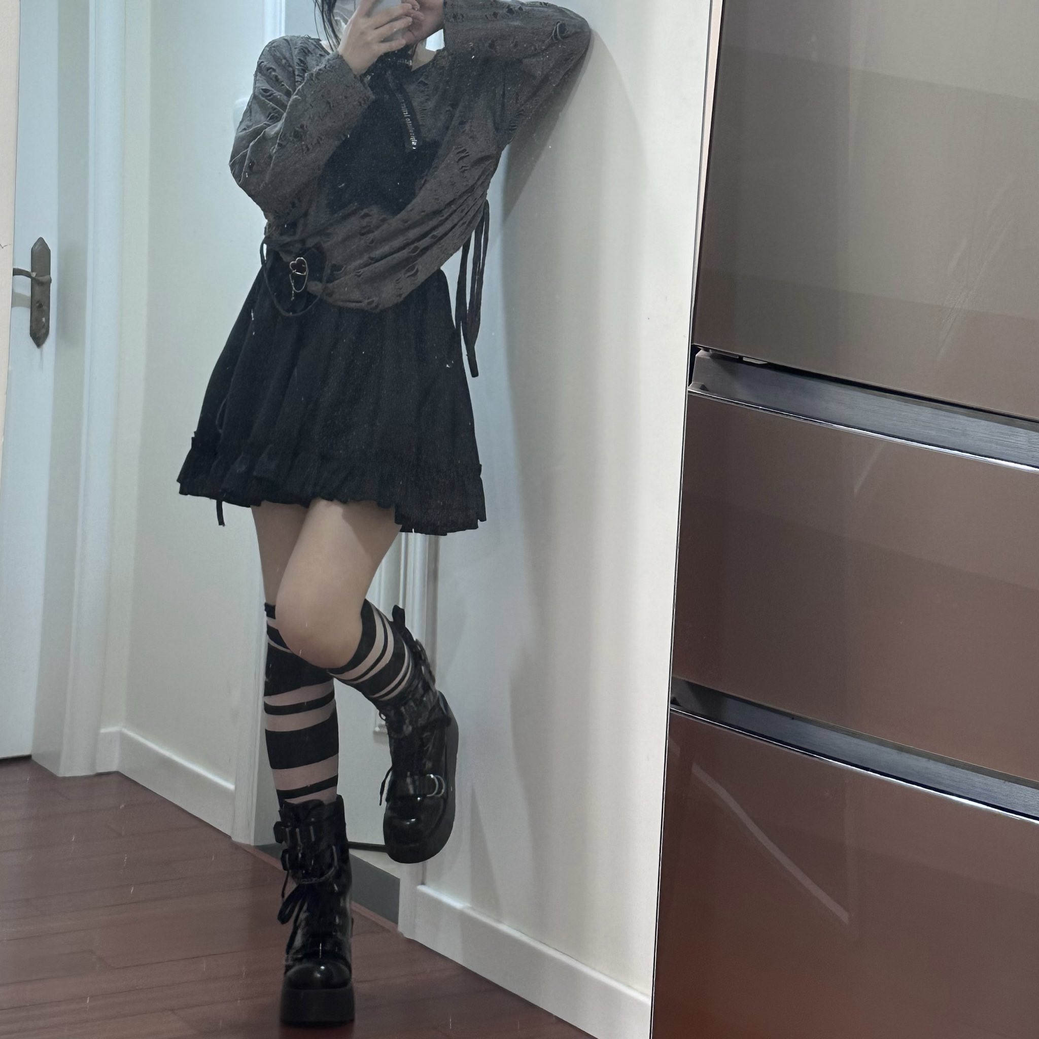 一位穿着黑色裙子和带条袜子的女人站在镜子前。