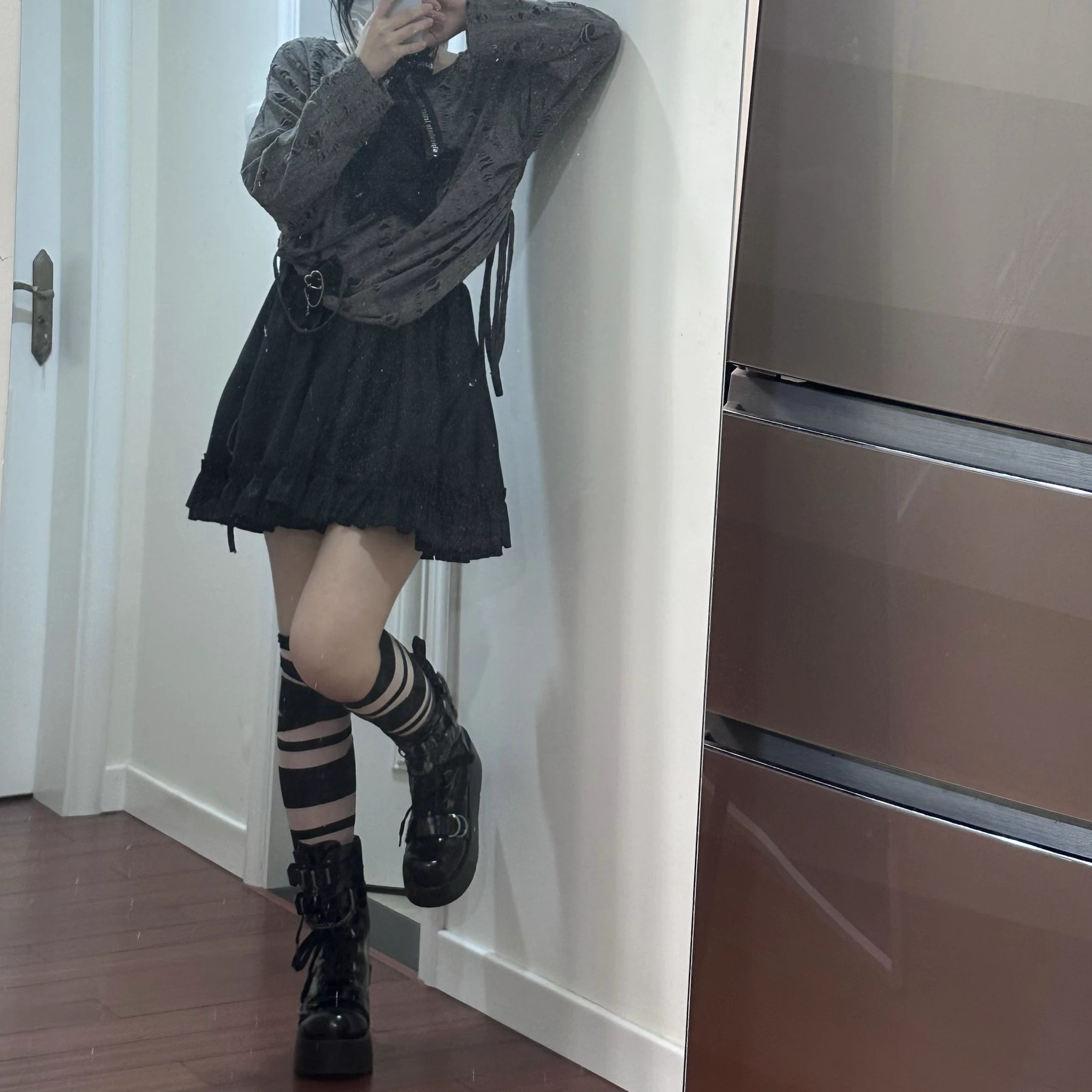 一位穿着黑色裙子和带条袜子的女人站在镜子前。