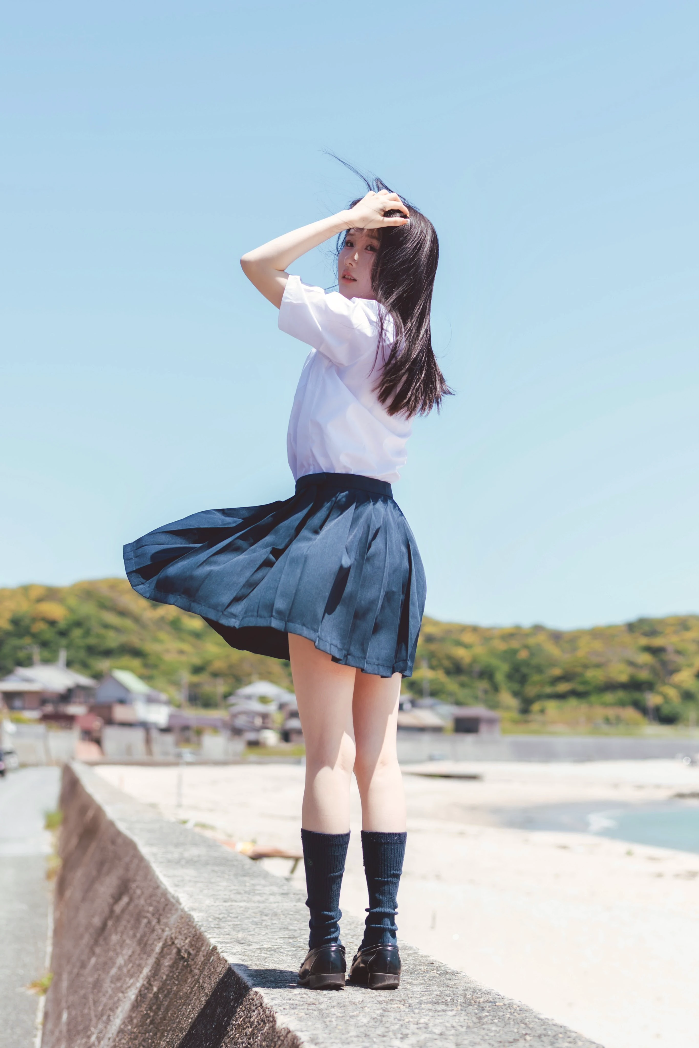 穿着蓝色裙子和白色衬衫的女人在海滩上露面。