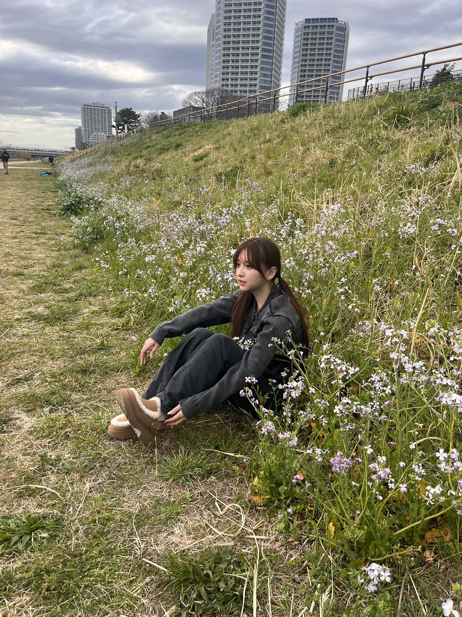 穿着灰色夹克的女人坐在一片花朵的田野里。