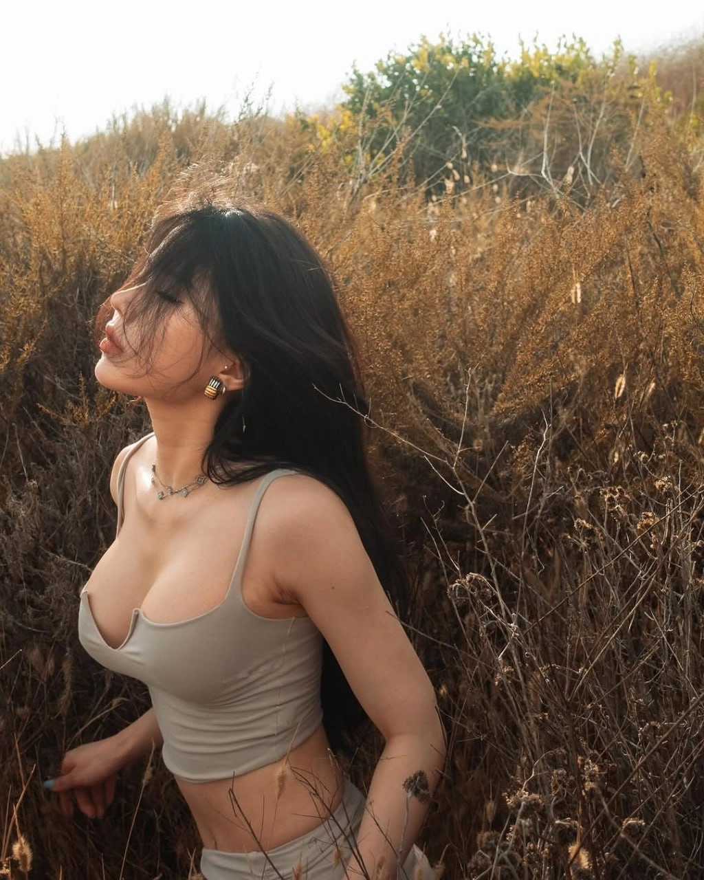 女人的纹身和一个大的胸部站在一个田野。