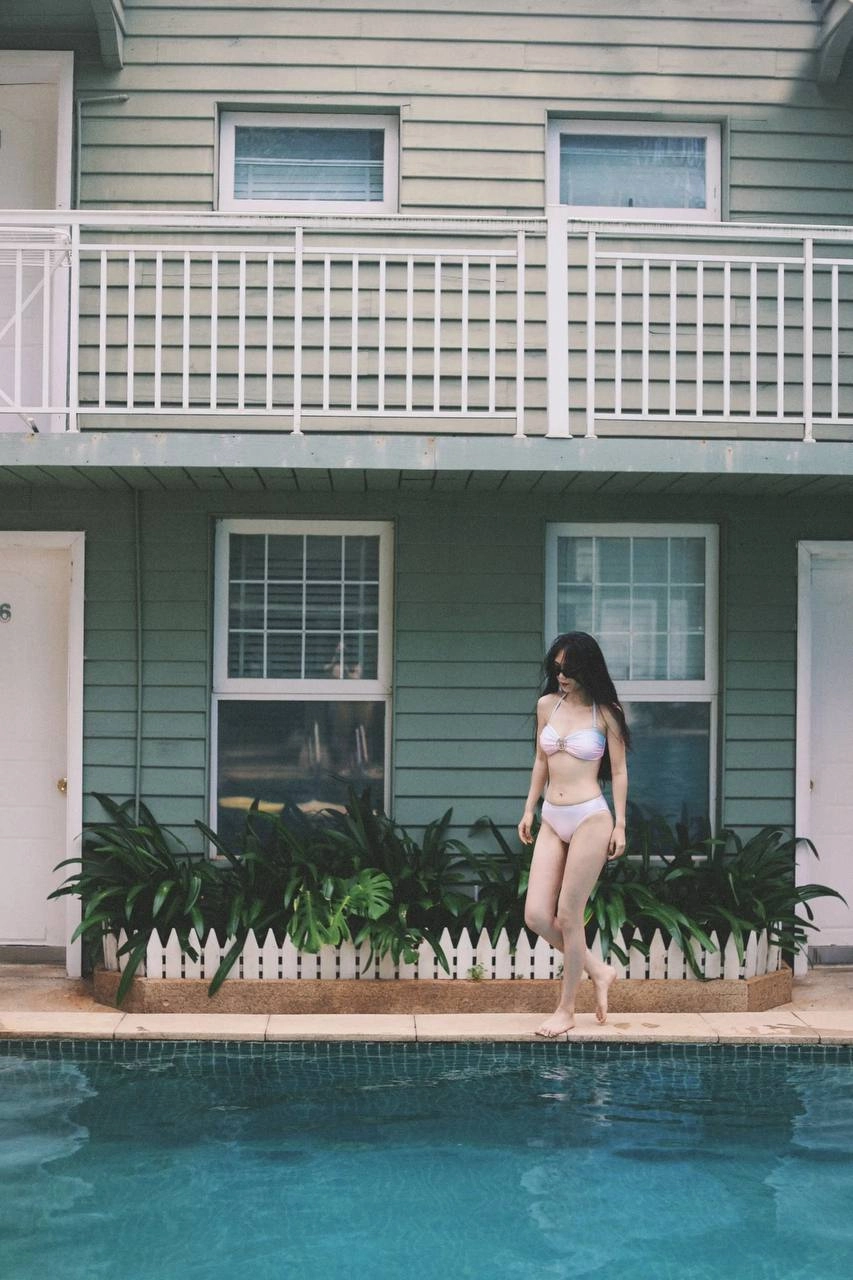 穿着白色比基尼顶和太阳镜的女人站在游泳池里。