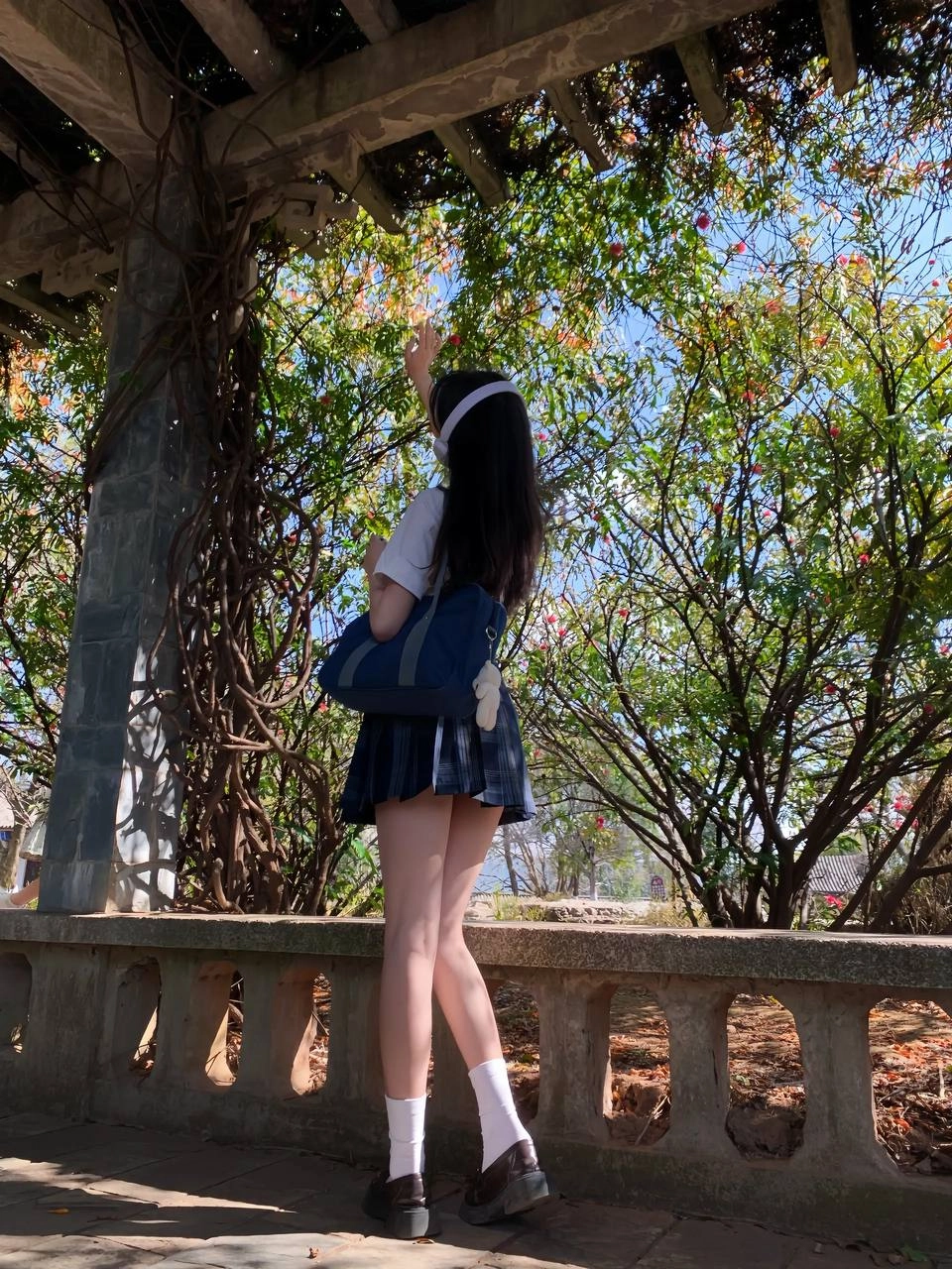 穿着白色衬衫和蓝色背包的女孩站在树下。