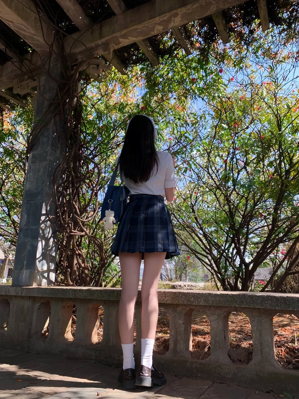 穿着白色衬衫和蓝色背包的女孩站在树下。