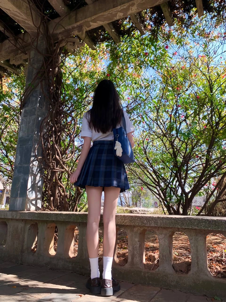 穿着白色衬衫和蓝色背包的女孩站在树下。