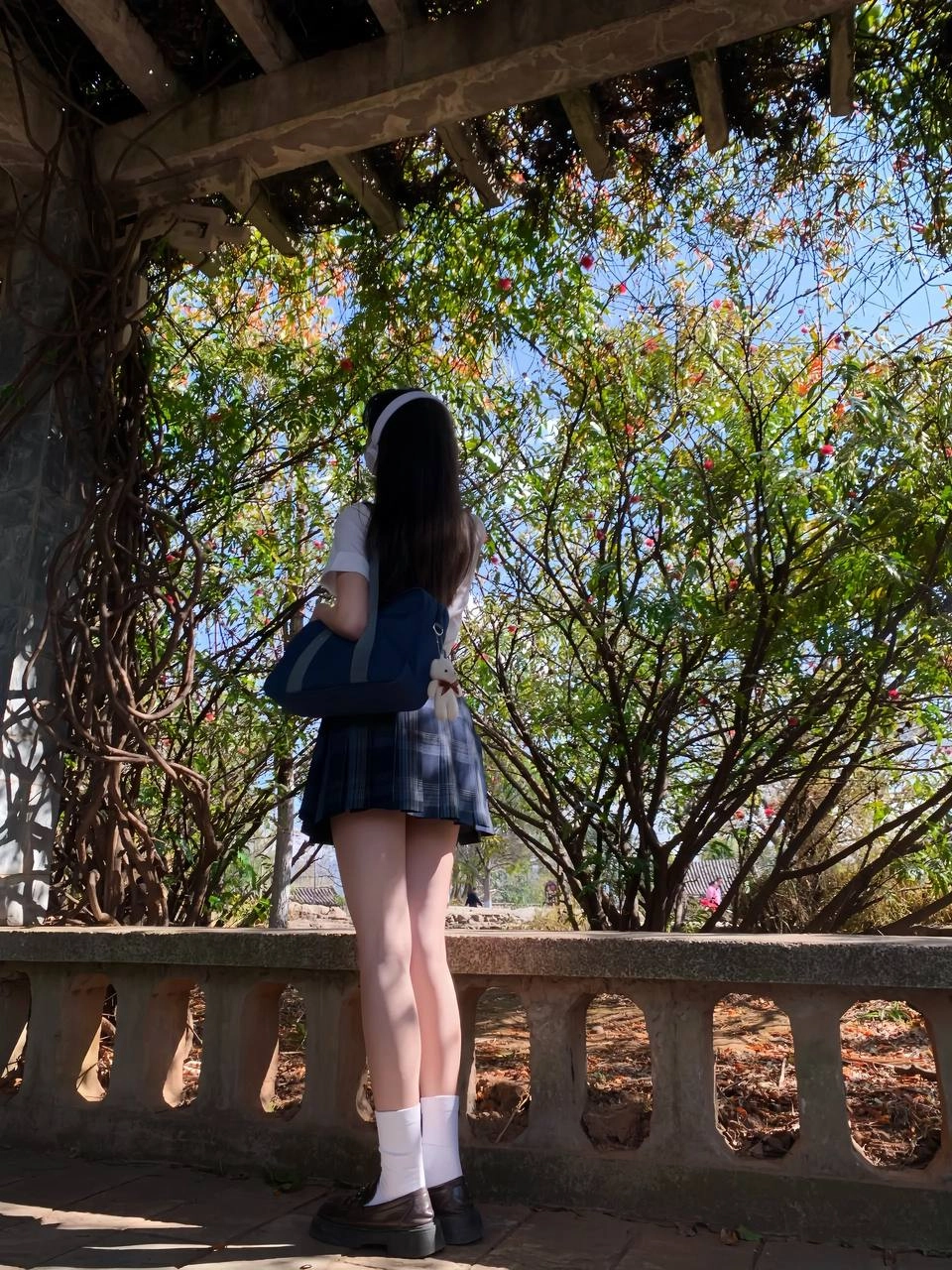 穿着白色衬衫和蓝色背包的女孩站在树下。