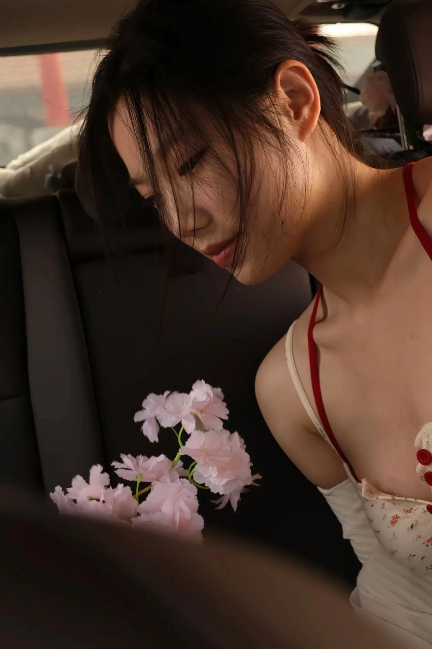 长头发和红色裙子的女人坐在一辆车里,一束粉红色的花朵。