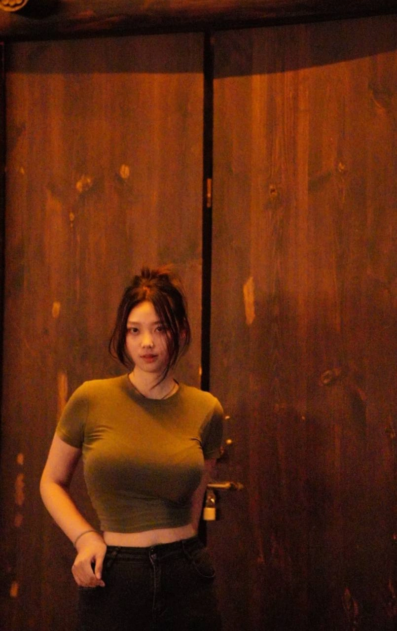 穿着绿色衬衫的女人站在一扇木门前。