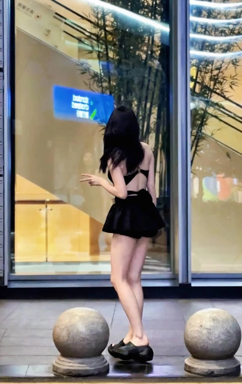 一位穿着黑色裙子和黑色胸罩的女人站在窗前。