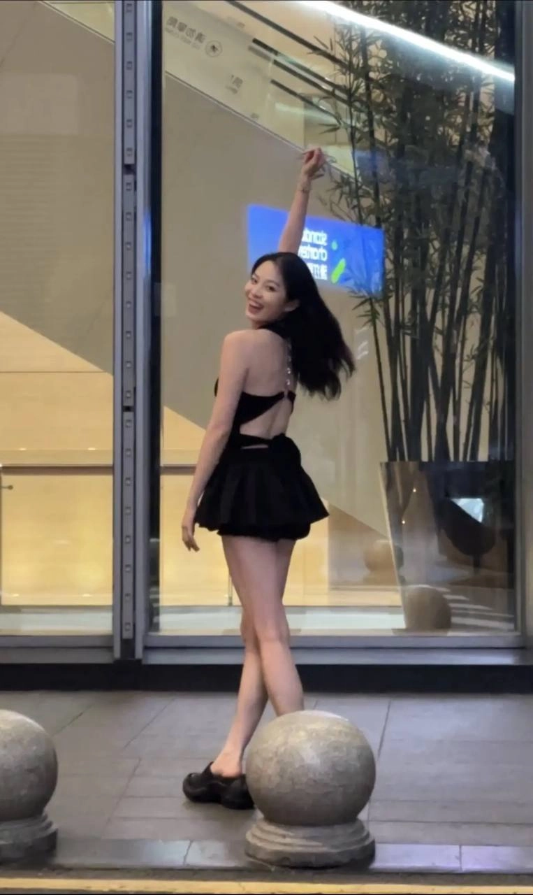 一位穿着黑色裙子和黑色胸罩的女人站在窗前。