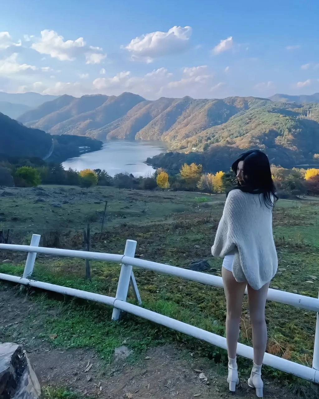 一位穿着白色衬衫的女人站在一堵墙上,俯瞰着一座湖泊。