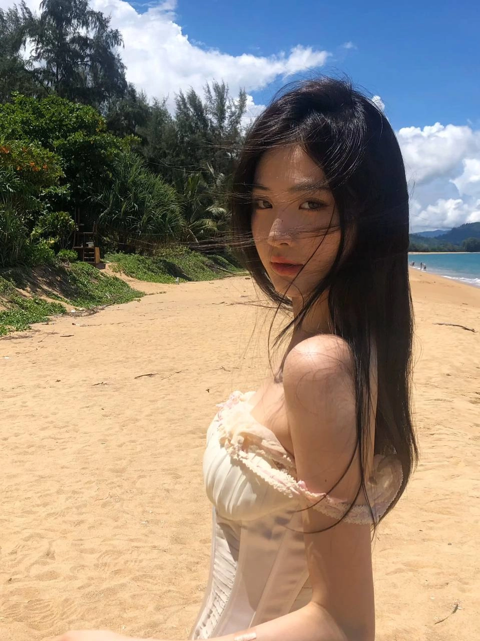 长头发和白色裙子的女人站在海滩上。