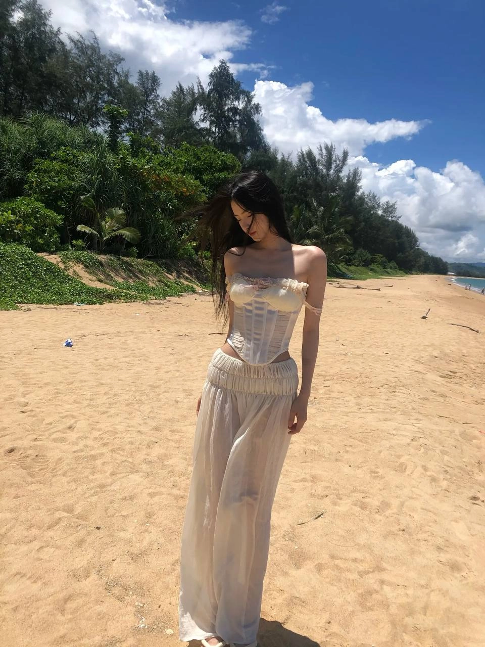 长头发和白色裙子的女人站在海滩上。