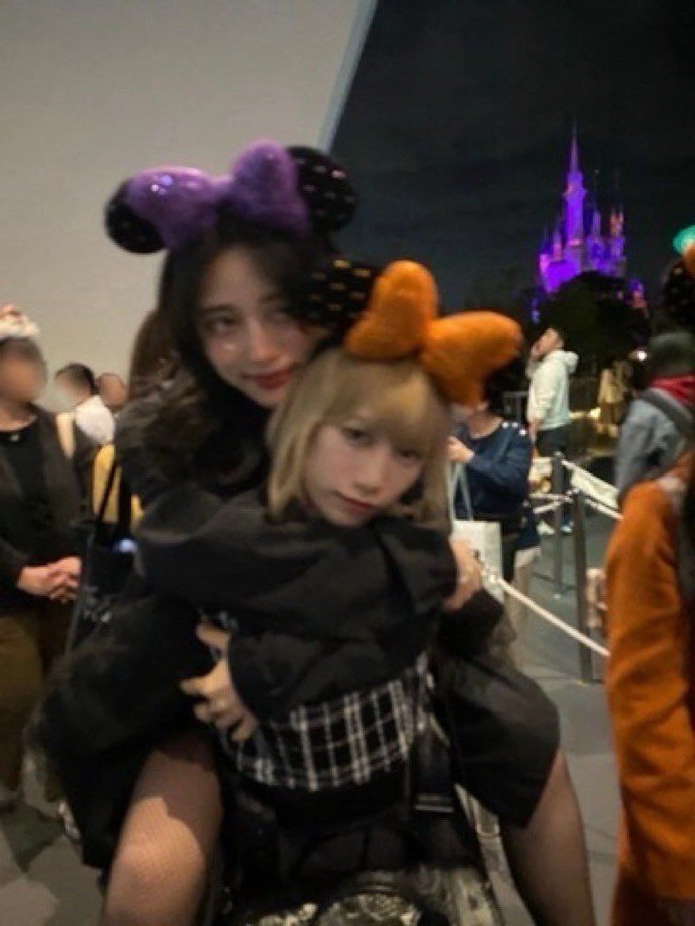 两个女孩戴着米妮小鼠的耳朵互相拥抱。