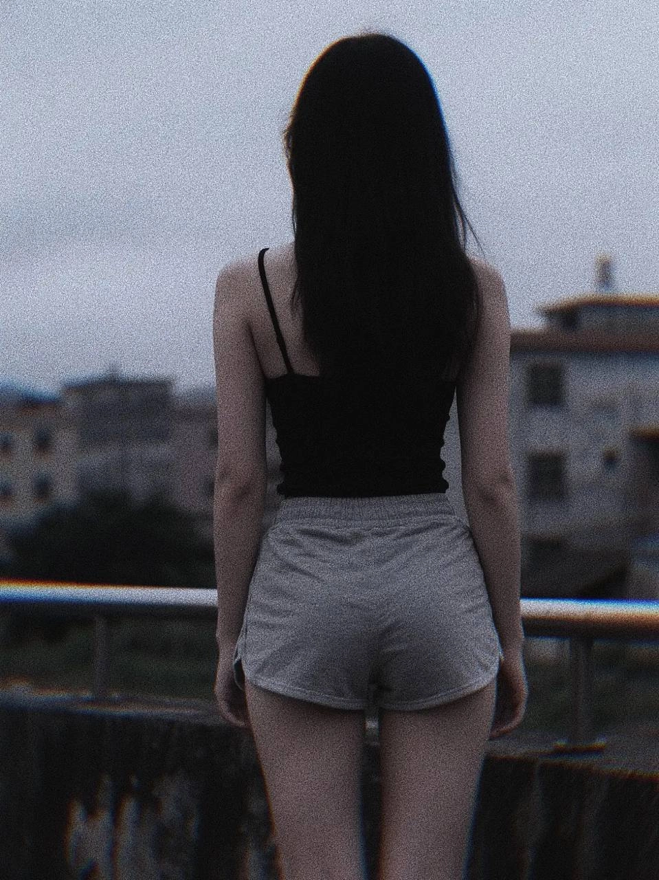 长头发和黑色坦克顶的女人站在桥上。