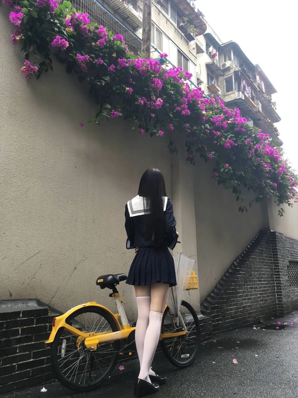 一位穿着蓝色裙子的女人站在一辆黄色的自行车旁边。