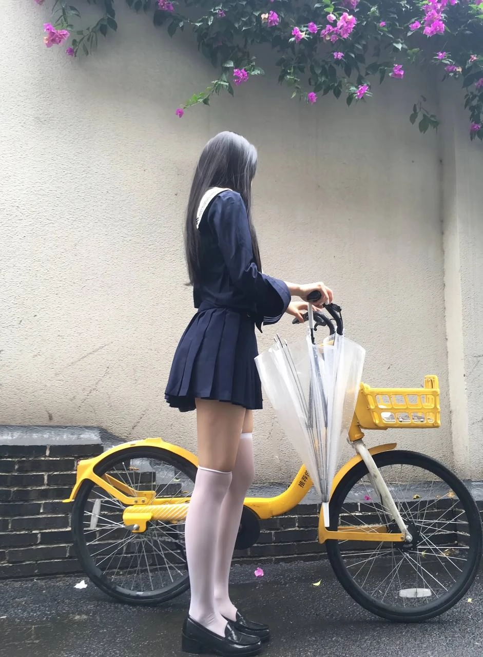 一位穿着蓝色裙子的女人站在一辆黄色的自行车旁边。