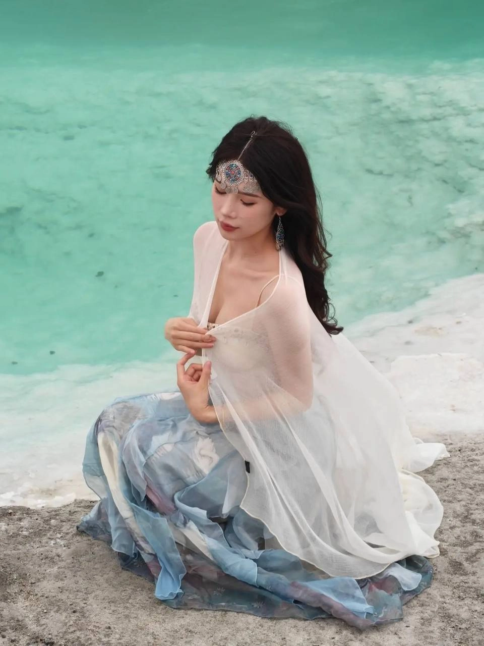 穿着白色裙子和头带的女人坐在水边。