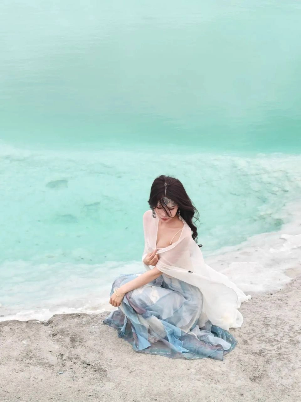 穿着白色裙子和头带的女人坐在水边。