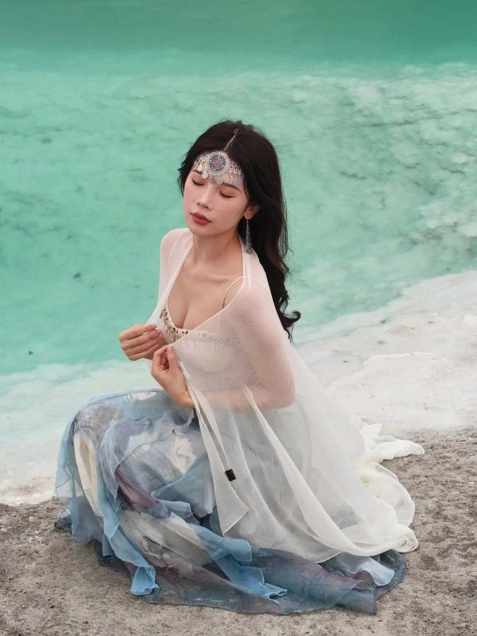 穿着白色裙子和头带的女人坐在水边。