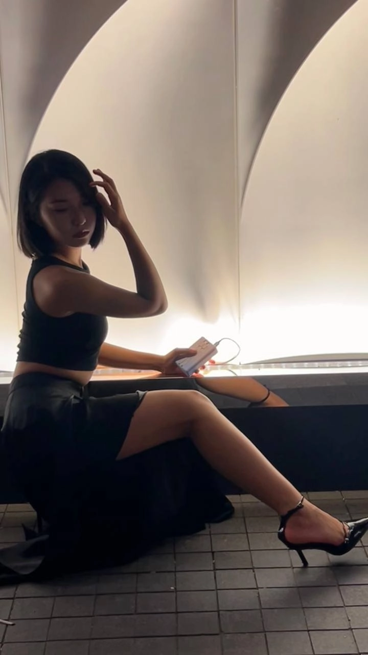 穿着黑色衬衫和黑色裙子的女人坐在一个凳子上。