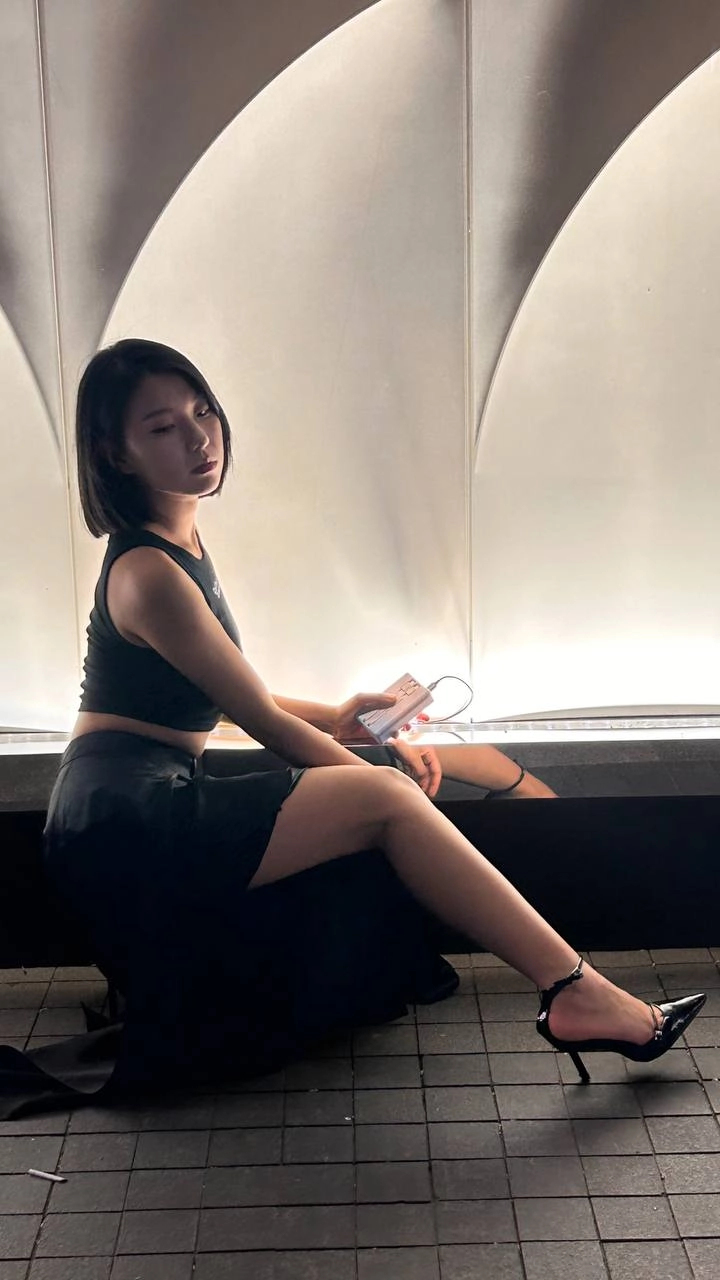 穿着黑色衬衫和黑色裙子的女人坐在一个凳子上。