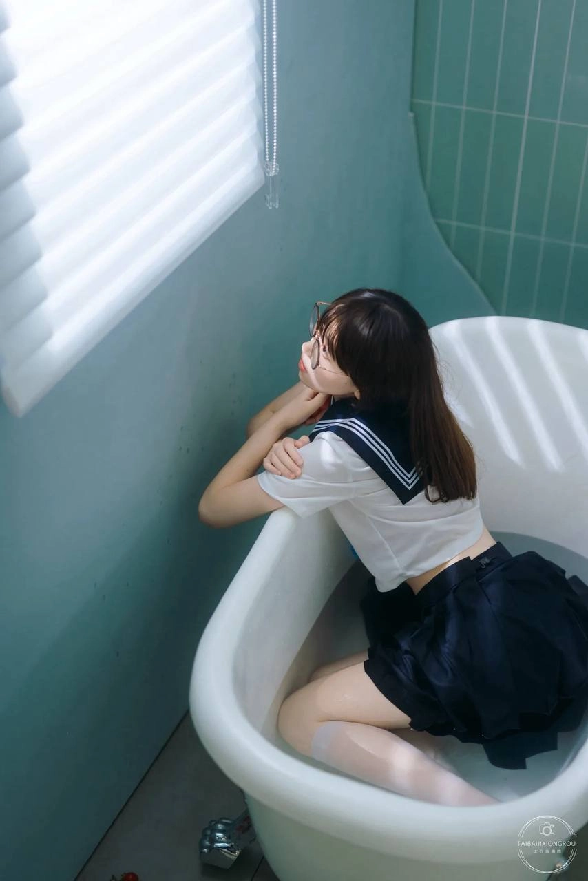 穿着白色衬衫和黑色裙子的女孩坐在浴缸里。