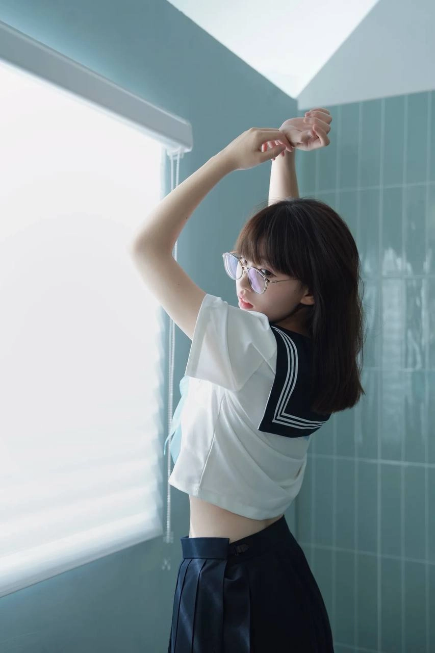 戴着眼镜和蓝色和白色的衬衫的女人坐在浴缸里。