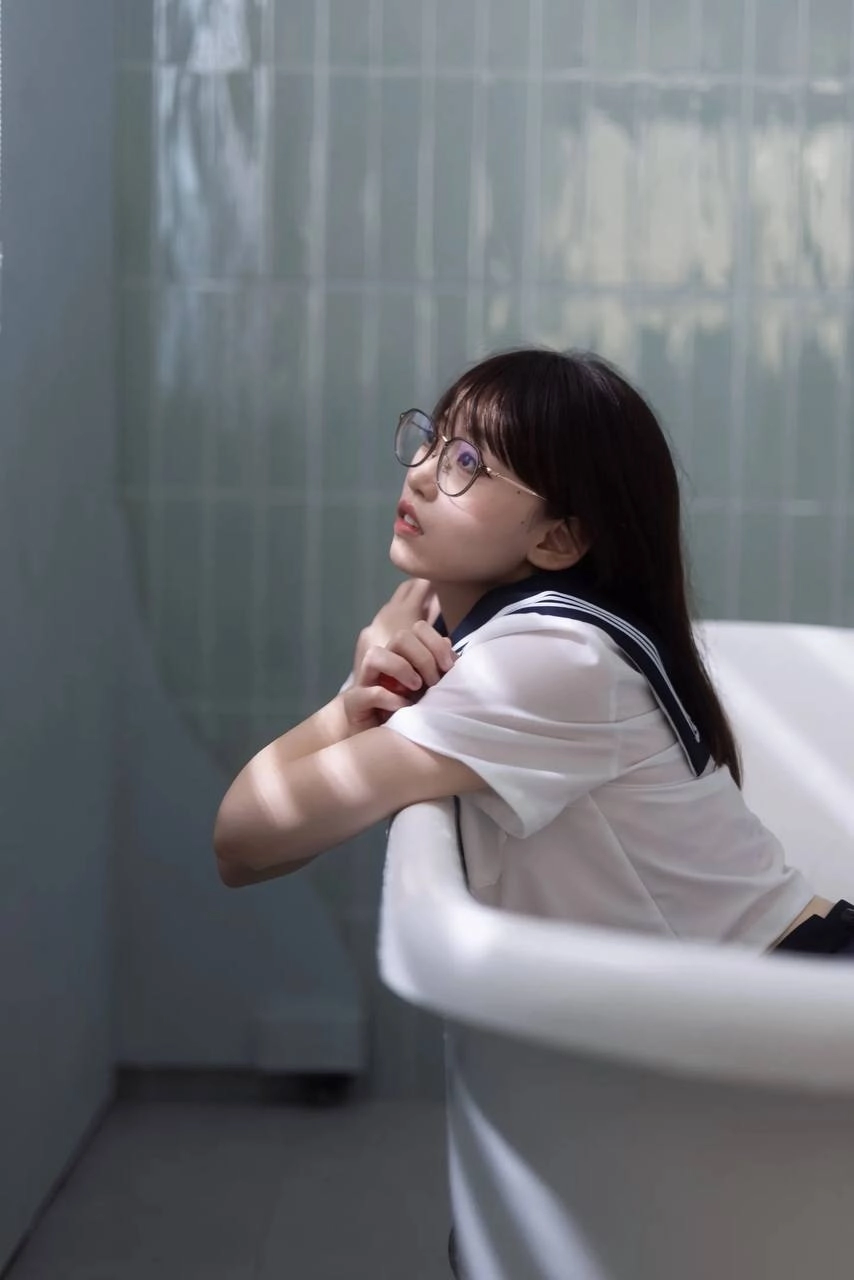 戴着眼镜和蓝色和白色的衬衫的女人坐在浴缸里。