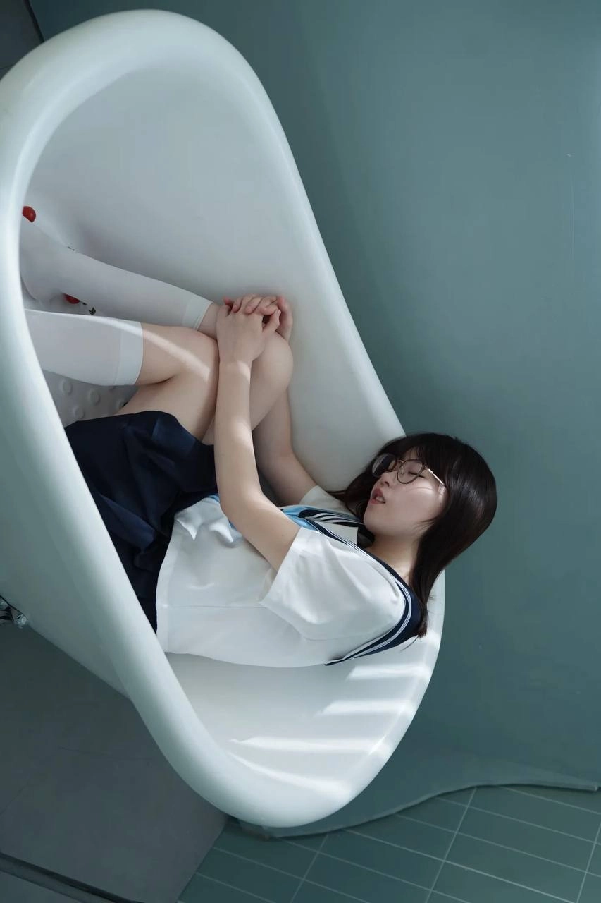 穿着白色衬衫和黑色裙子的女孩坐在浴缸里。