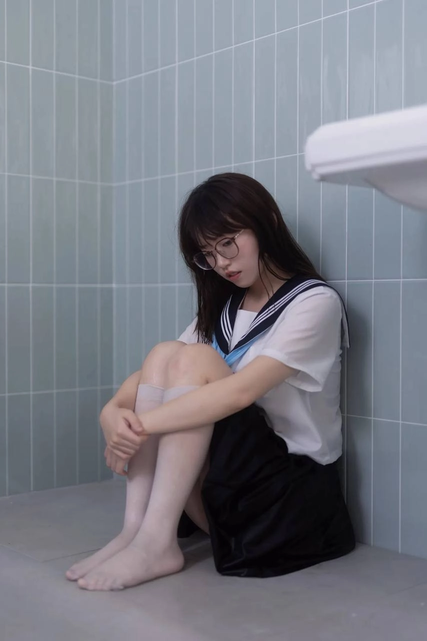 戴着眼镜和蓝色和白色的衬衫的女人坐在浴缸里。