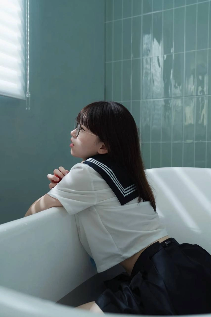 穿着白色衬衫和黑色裙子的女孩坐在浴缸里。