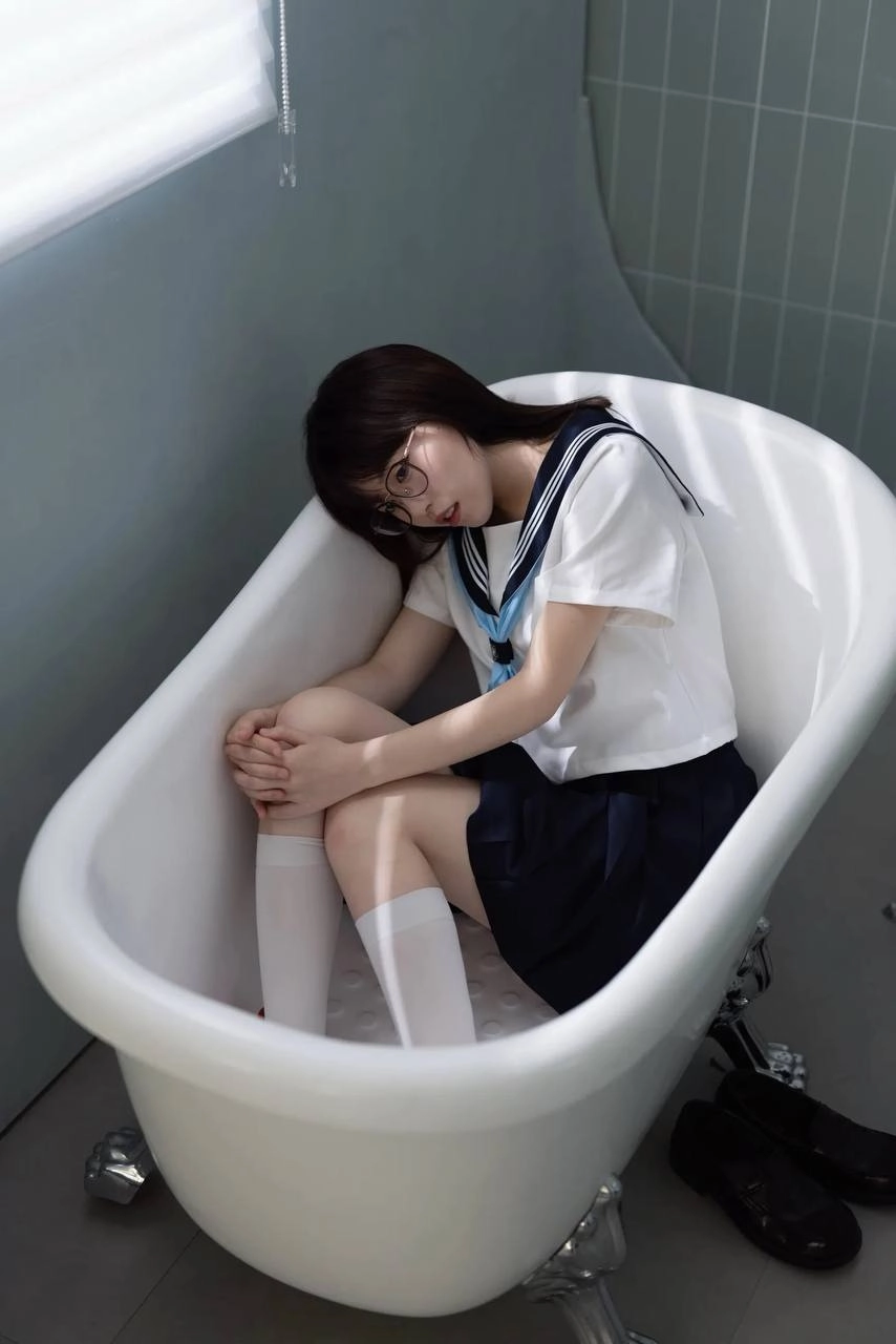 穿着白色衬衫和蓝色领带的女人坐在浴缸里。