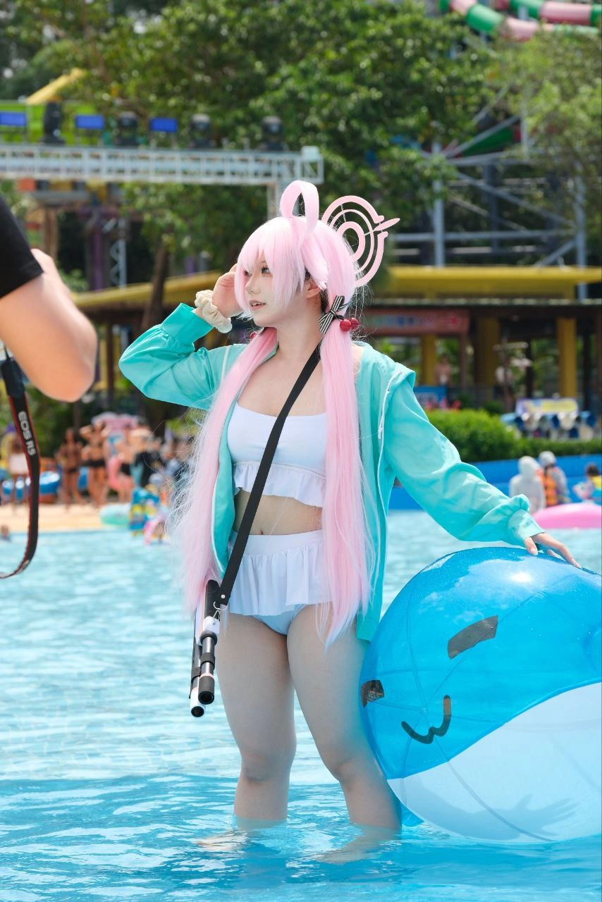 穿着粉红色毛衣和白色泳衣的女人拿着一个蓝色的球。