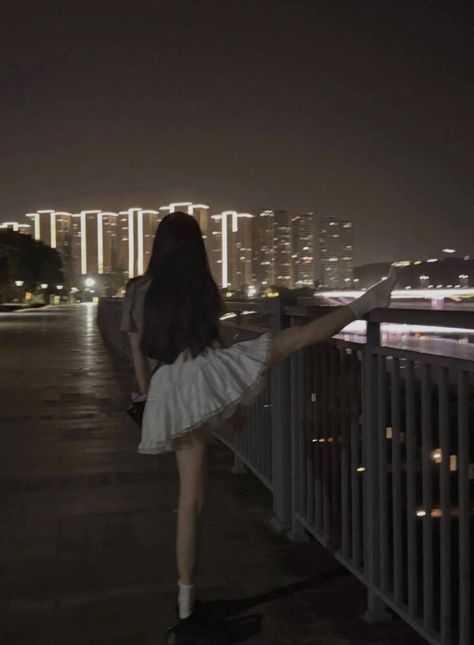 一位穿着白色衣服和黑色鞋子的女人站在一座桥上。