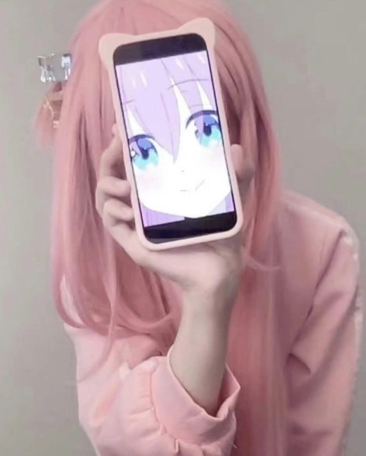 粉红发的女孩拿着手机,上面有一张卡通脸。