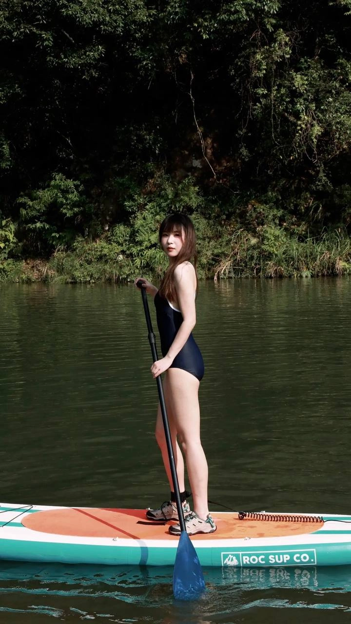 一位穿着黑色和蓝色的泳衣的女人站在水中冲浪板上。