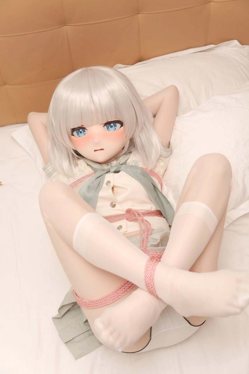 一只带蓝色弓绳和白头发的娃娃躺在床上。