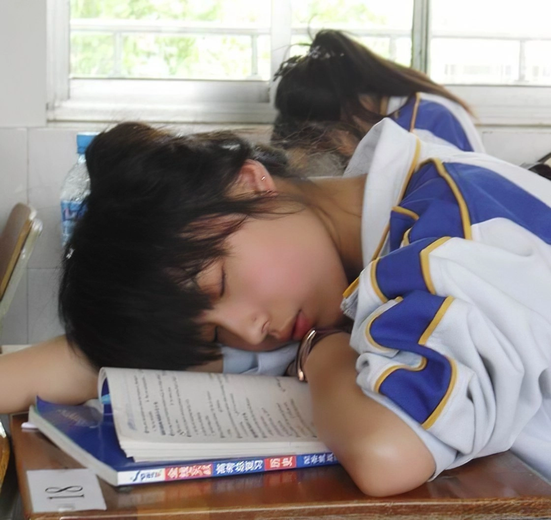 女孩睡在一张桌子上,上面有一本书。