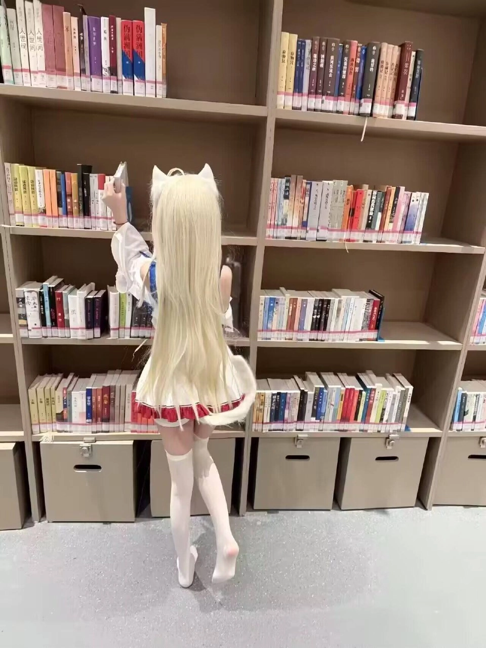 长发和白色裙子的女孩站在书架前面。