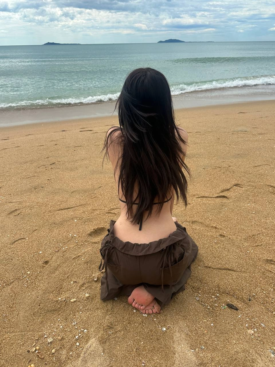 长头发的女人坐在海滩上。