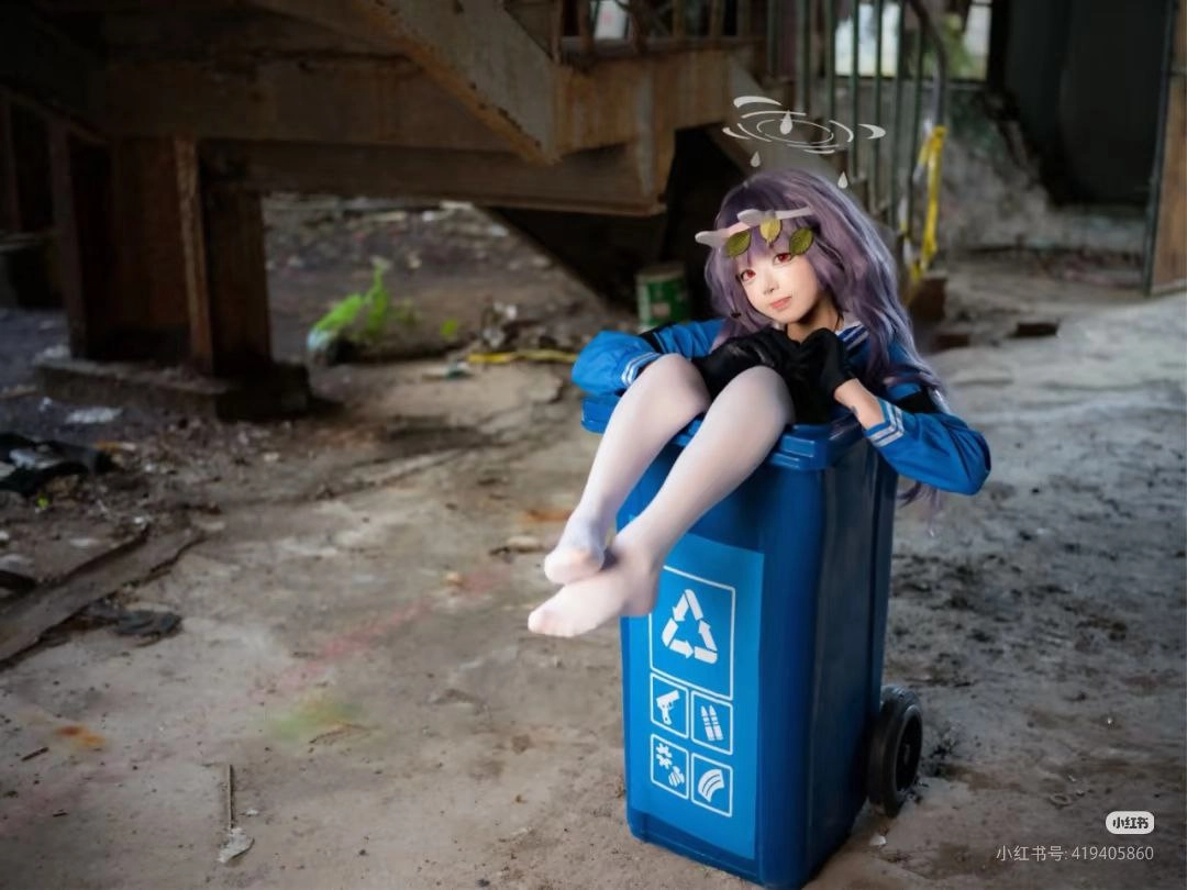 一位穿着蓝色夹克和黑色手套的女孩坐在蓝色垃圾桶里。