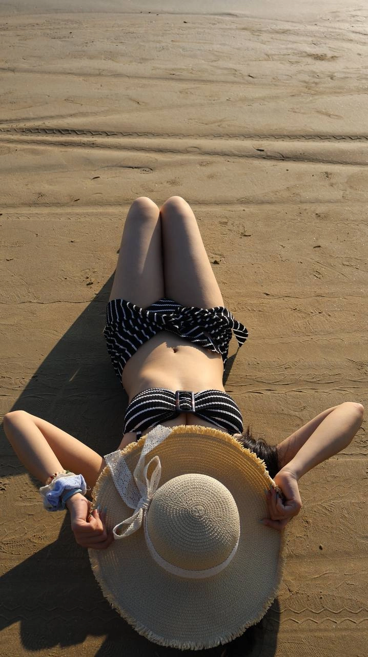 一位穿着比基尼顶和帽子的女人站在海滩上。