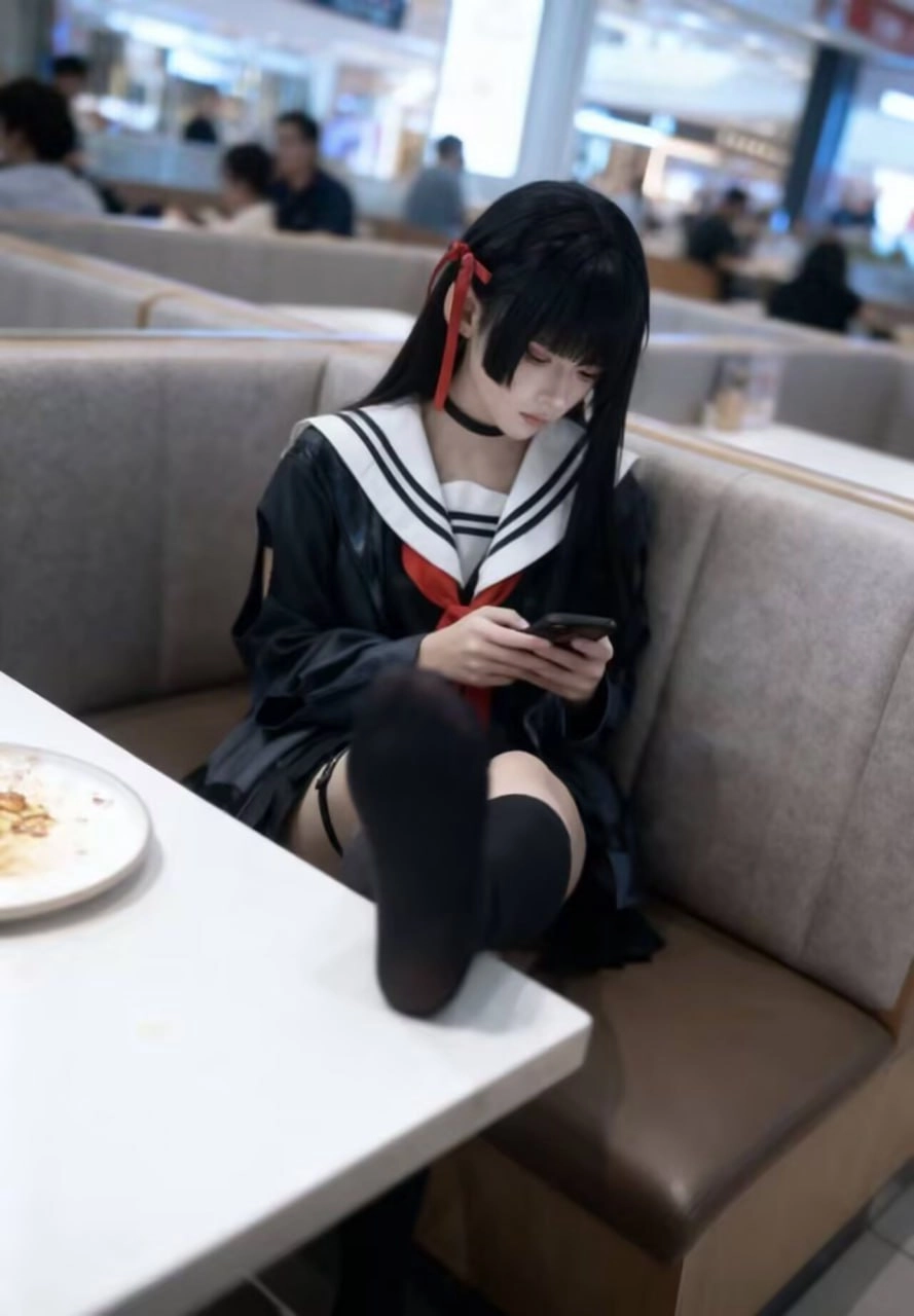 一位穿着黑色和红色的水手服的女孩坐在一张桌子上,看着她的手机。