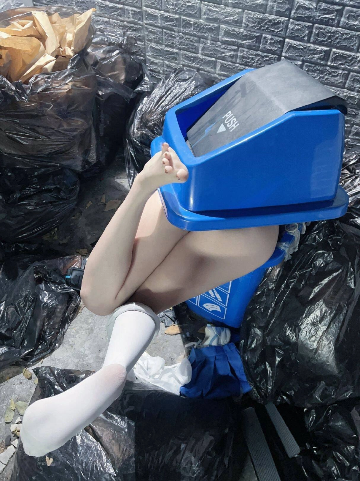 一位穿着蓝色衬衫和白色袜子的女孩坐在蓝色垃圾桶上。