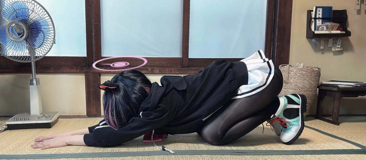 女人穿着黑色夹克和白色裙子跪在地板上。